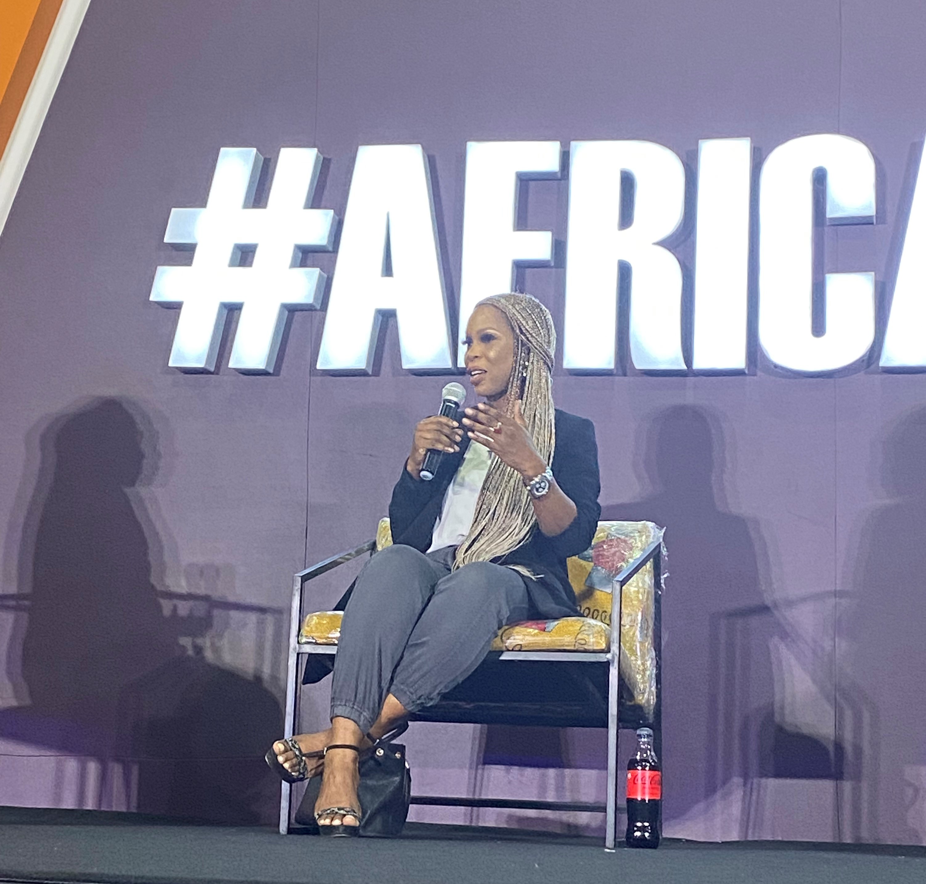 Ommo Clark seated on stage during a panel at Africa NXT in Lagos, 2022, holding a microphone